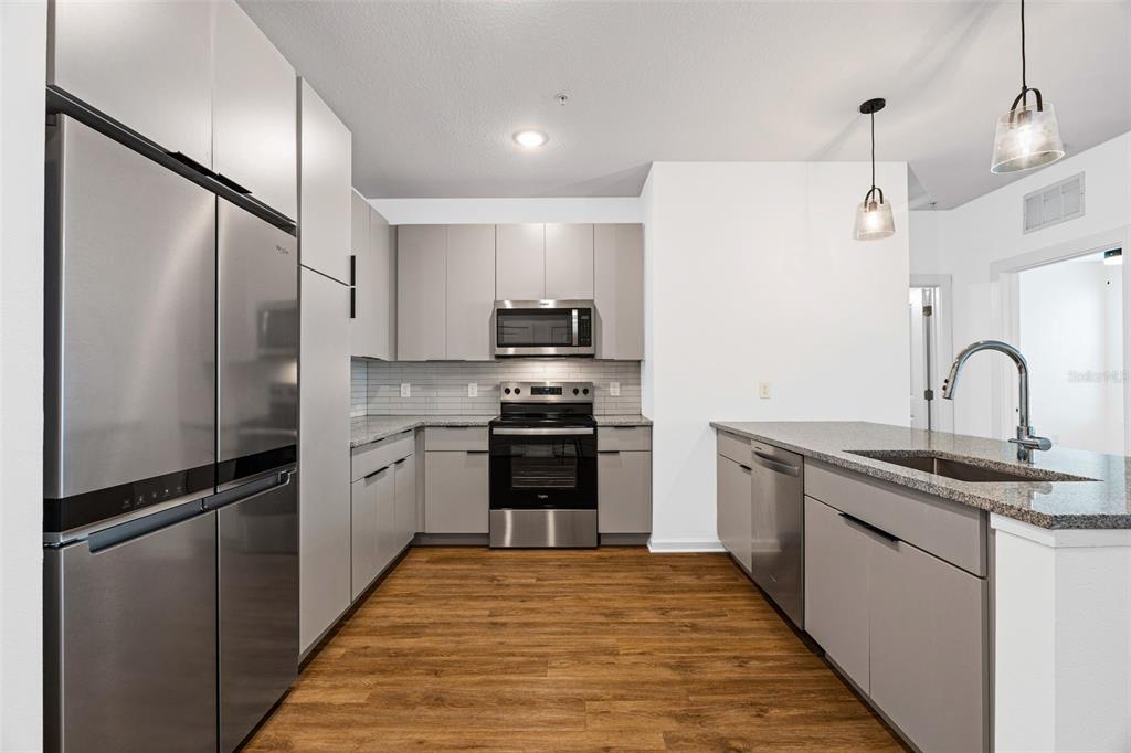A modern kitchen features stainless steel appliances, grey cabinetry, and a granite-topped island — 1700 RANCH ROAD UNIT B1-13112, NOKOMIS, FL