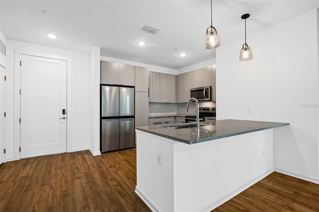 A modern kitchen features stainless steel appliances, gray cabinetry, granite countertops, and wood-look flooring — 1700 RANCH ROAD UNIT B1-13112, NOKOMIS, FL