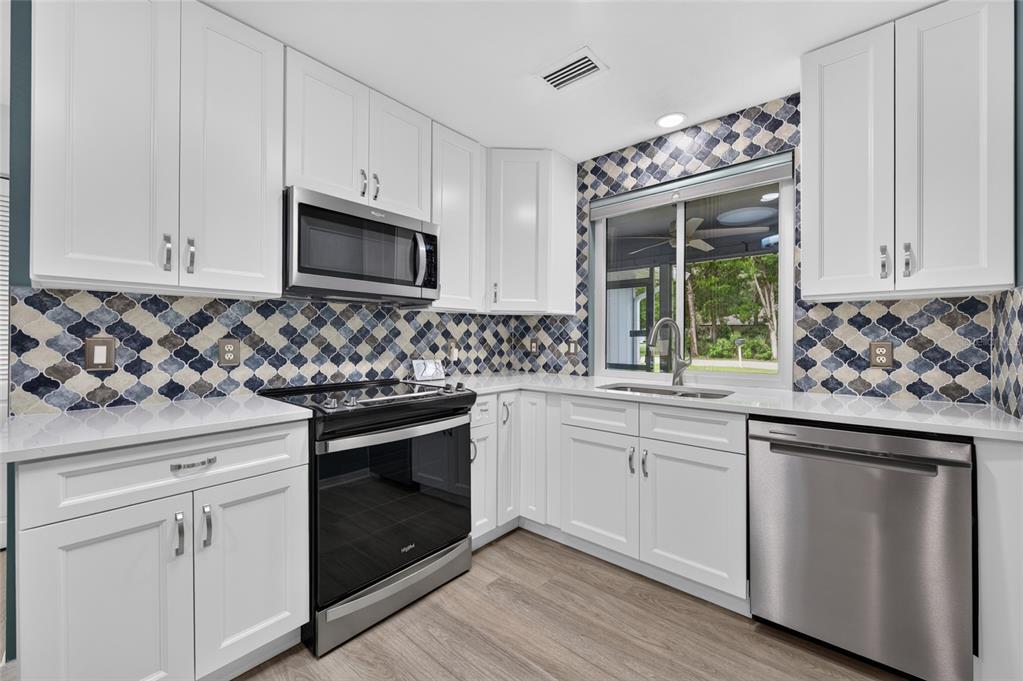 A kitchen with white cabinets, stainless steel appliances, and a patterned blue and white backsplash — 113 DUSK MEADOW TRAIL, PORT ORANGE, FL