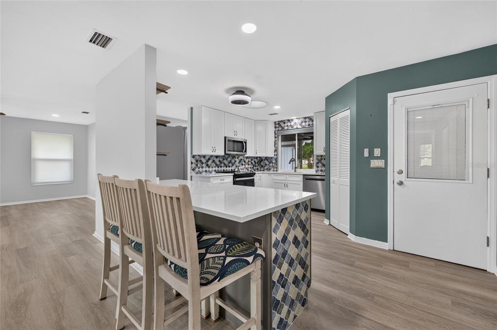 A kitchen with a white island, bar stools, patterned tile backsplash, and light wood flooring — 113 DUSK MEADOW TRAIL, PORT ORANGE, FL