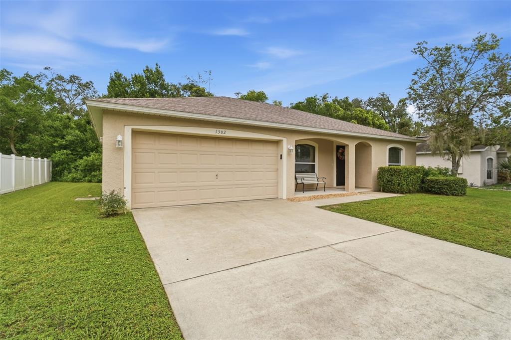 A single-story house with a beige stucco exterior, a two-car garage, and a concrete driveway — 1302 BENTON LAKE DRIVE E, DELAND, FL