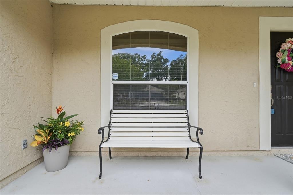 A white metal bench sits on a concrete porch in front of a window — 1302 BENTON LAKE DRIVE E, DELAND, FL