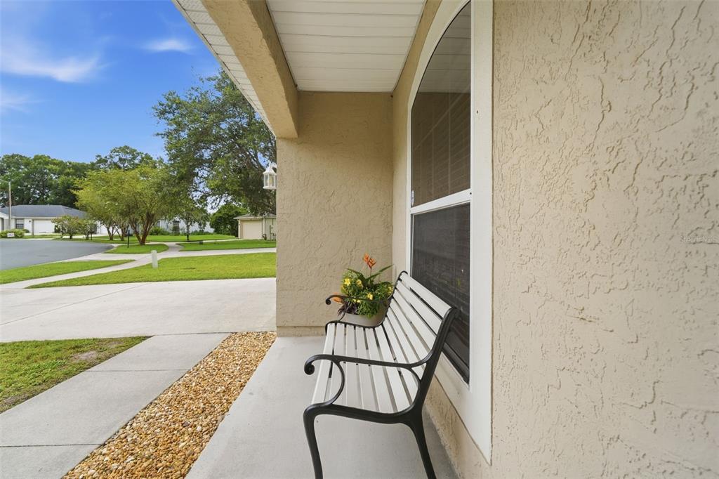 A white metal bench sits on a concrete porch next to a house exterior wall — 1302 BENTON LAKE DRIVE E, DELAND, FL