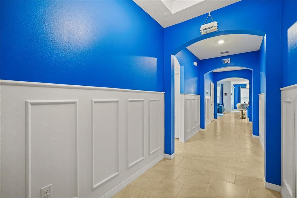 A hallway with bright blue walls, white wainscoting, and tile flooring leads to an open area — 1967 RANKIN ST, KISSIMMEE, FL