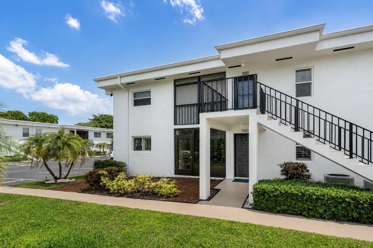 Exterior view of a two-story white apartment building with an outdoor staircase and landscaping — 14897 Bal Moral Lane # 105, Delray Beach FL 33446, DELRAY BEACH, FL