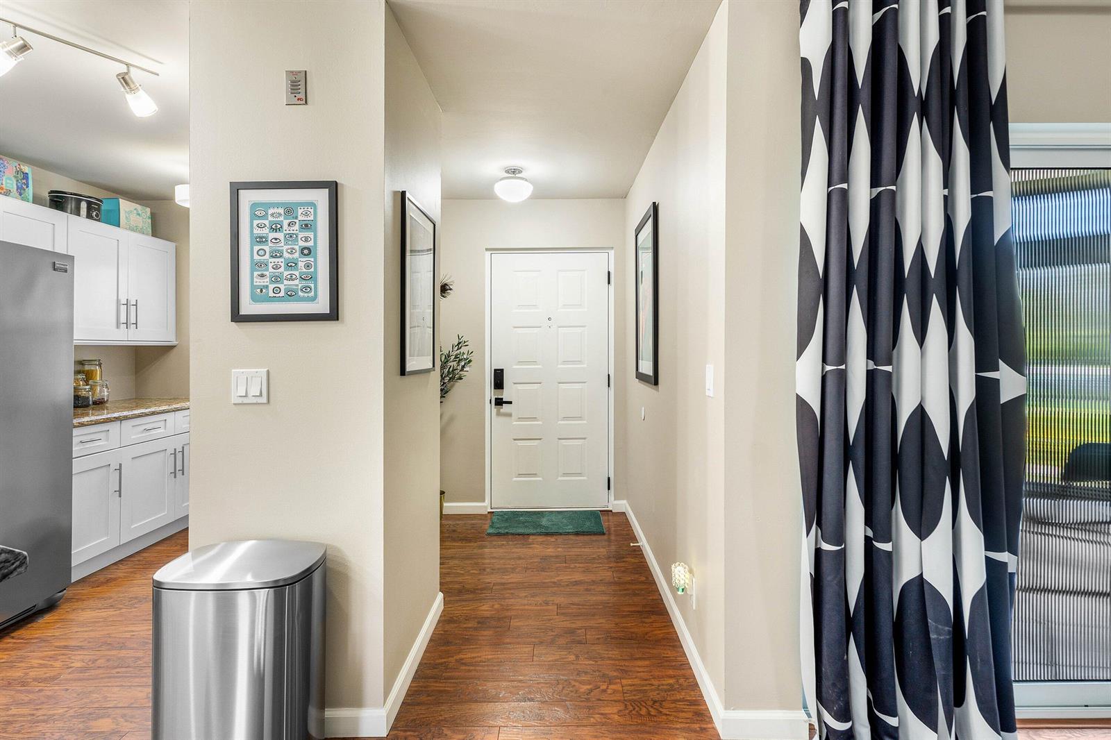A hallway with wood-look flooring leads to a white front door near a kitchen area — 14897 Bal Moral Lane # 105, Delray Beach FL 33446, DELRAY BEACH, FL