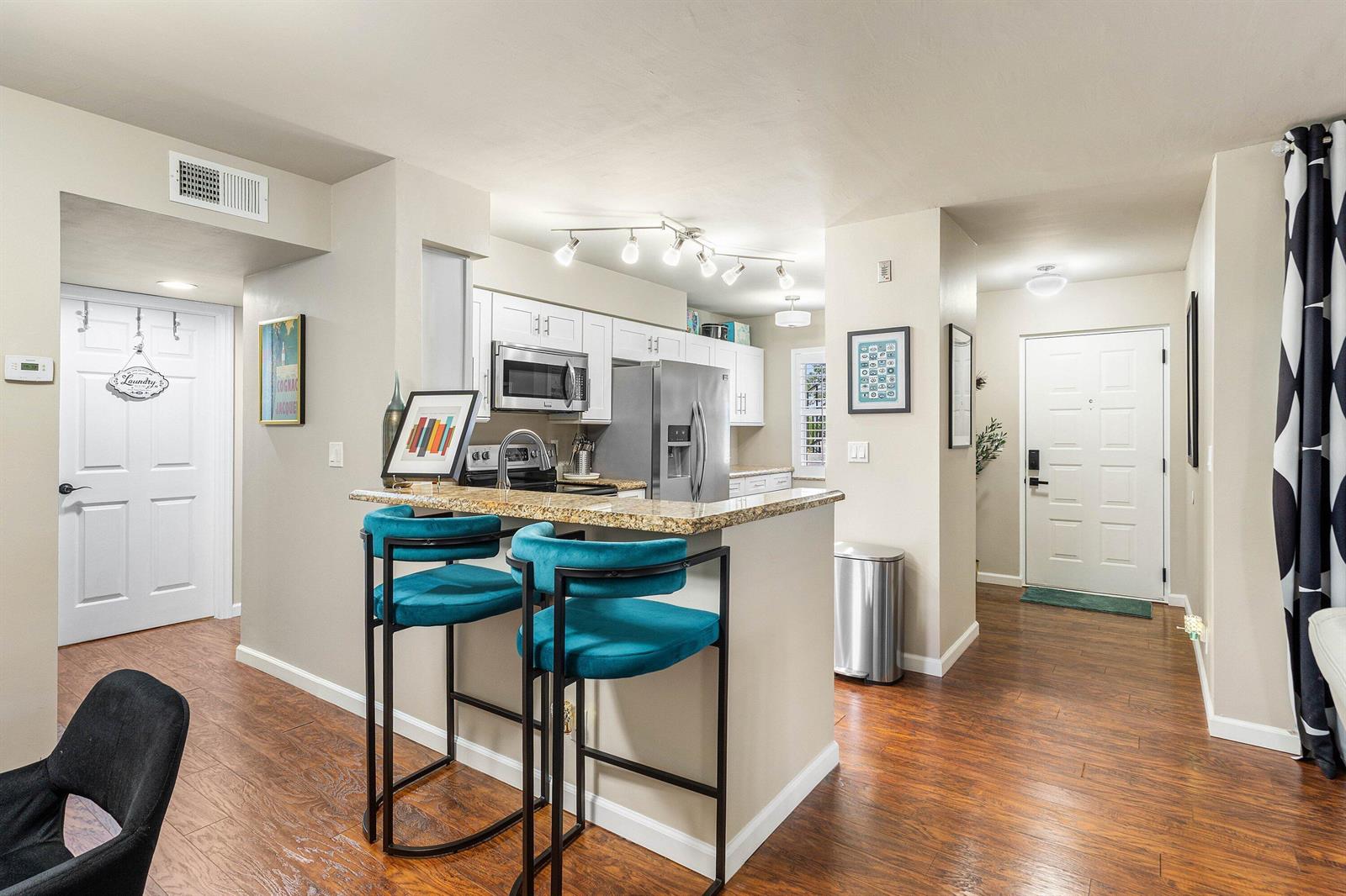 A kitchen with white cabinets, granite countertops, and two teal bar stools on wood flooring — 14897 Bal Moral Lane # 105, Delray Beach FL 33446, DELRAY BEACH, FL