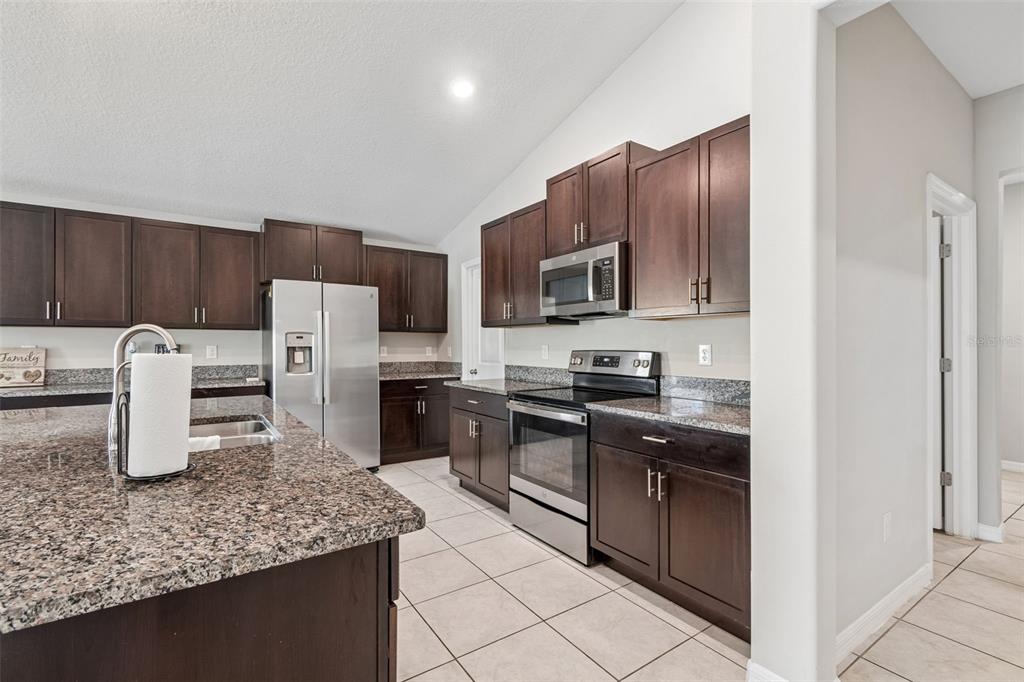 A kitchen features dark wood cabinets, granite countertops, stainless steel appliances, and tile flooring — 1565 COLDING DRIVE, RUSKIN, FL