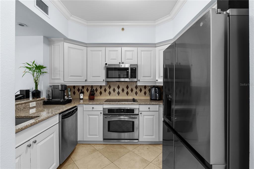 A kitchen features white cabinetry, granite countertops, stainless steel appliances, and a diamond-patterned tile backsplash — 7593 GATHERING DRIVE UNIT 307, KISSIMMEE, FL