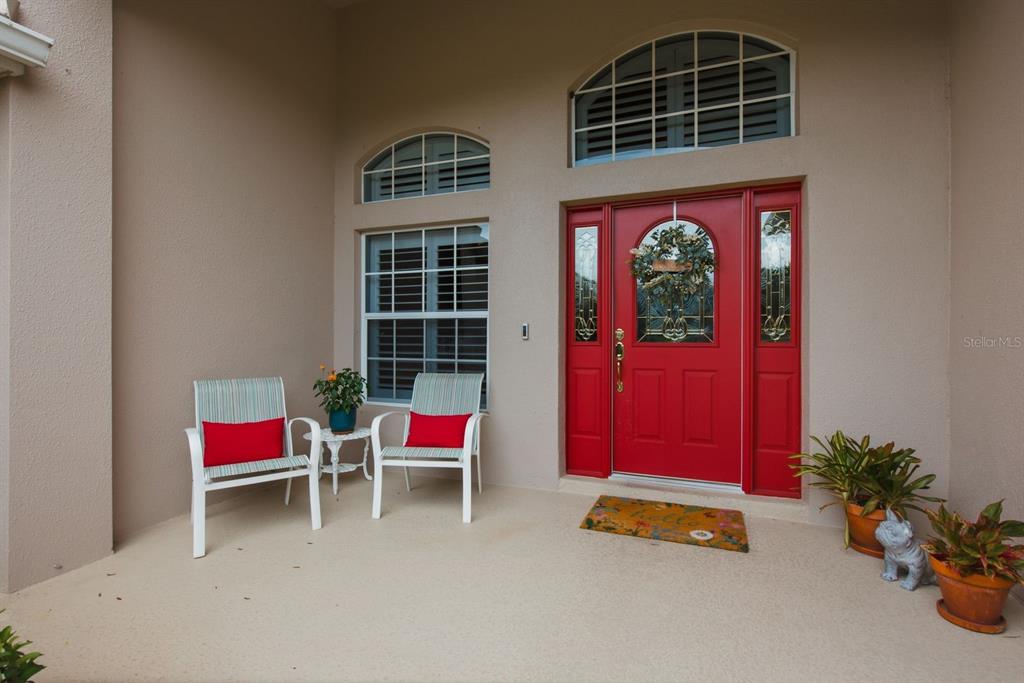 A covered front porch features a bright red door, two chairs, and potted plants — 3900 LIBERTY HILL DRIVE, CLERMONT, FL