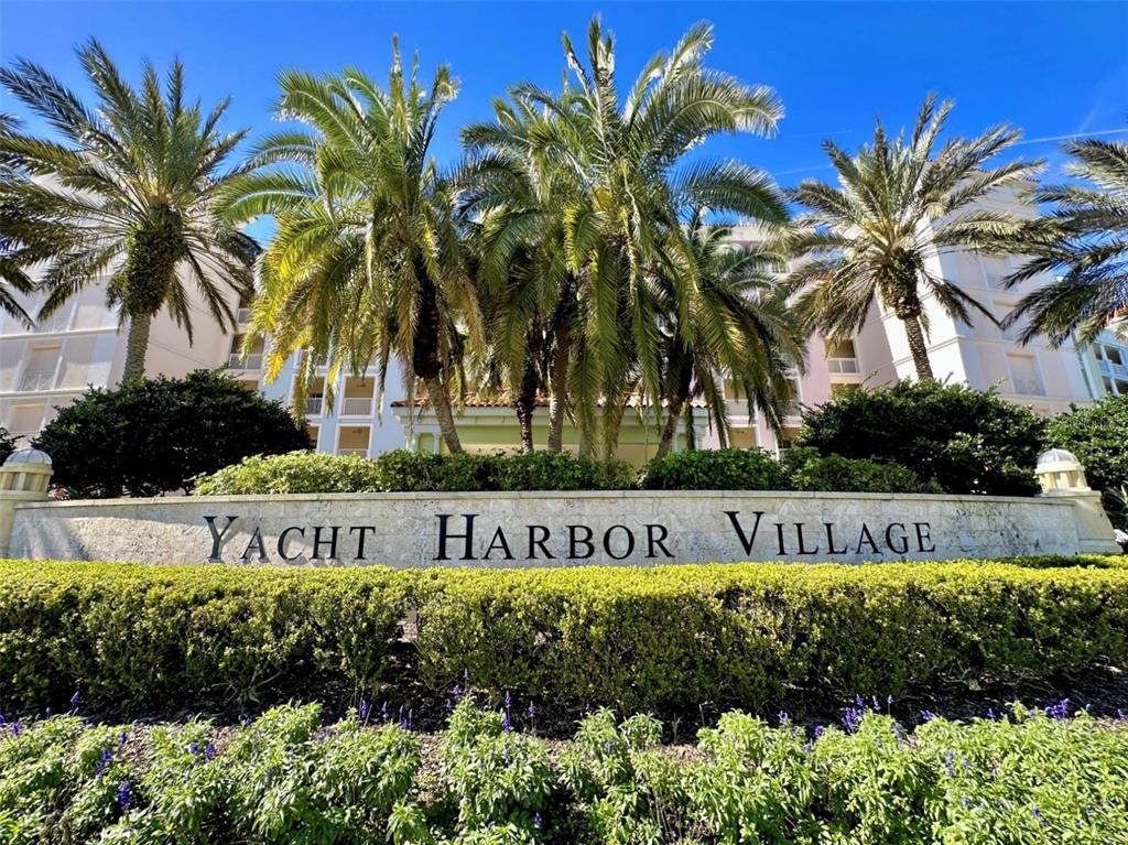 A stone sign reading Yacht Harbor Village sits in front of palm trees and a building — 244 HARBOR VILLAGE POINT N, PALM COAST, FL