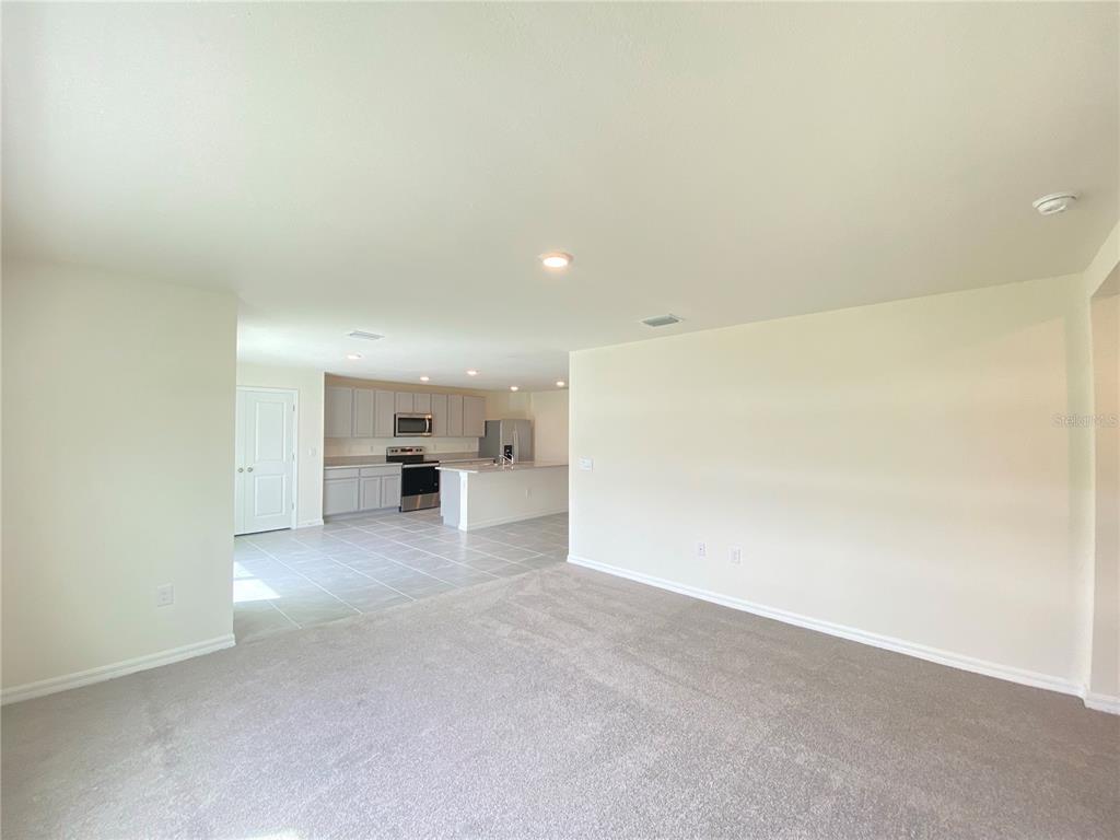 An open-concept living area with gray carpet leads to a kitchen with light-colored cabinets — 2113 NW 247 DRIVE, NEWBERRY, FL