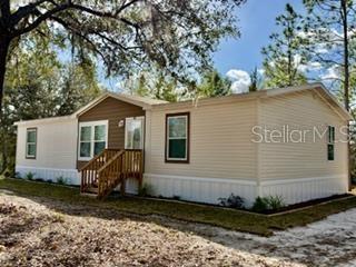A beige manufactured home with brown siding accents and a wooden staircase sits outdoors — 2629 NW 29TH TERRACE, BELL, FL