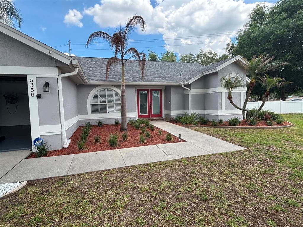 A gray single-story house features a red double front door and a palm tree — 5358 MONTSERRAT DRIVE, LAKELAND, FL