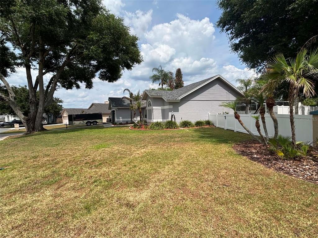 A grassy yard extends toward a gray house with a white fence and palm trees — 5358 MONTSERRAT DRIVE, LAKELAND, FL