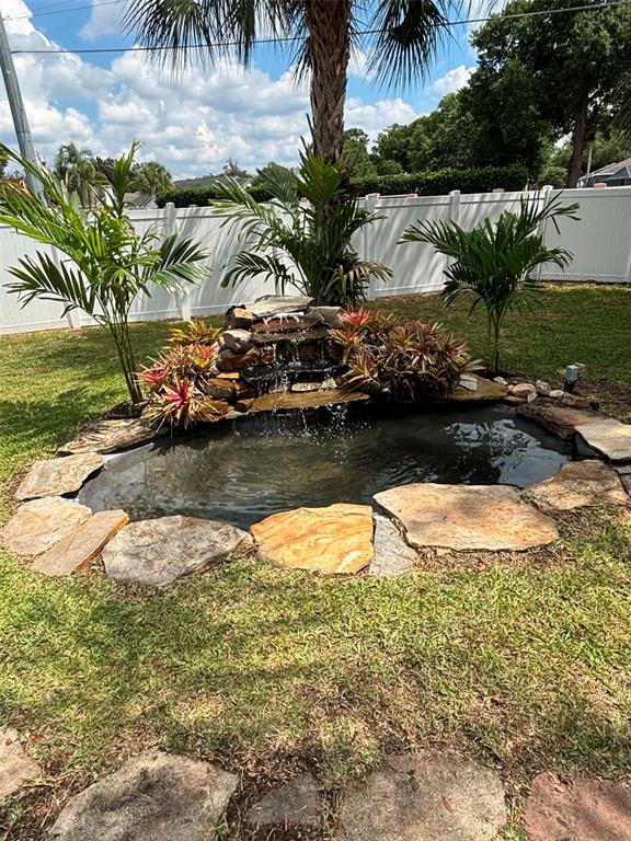 A backyard pond with a stone waterfall feature is surrounded by palm trees and landscaping — 5358 MONTSERRAT DRIVE, LAKELAND, FL