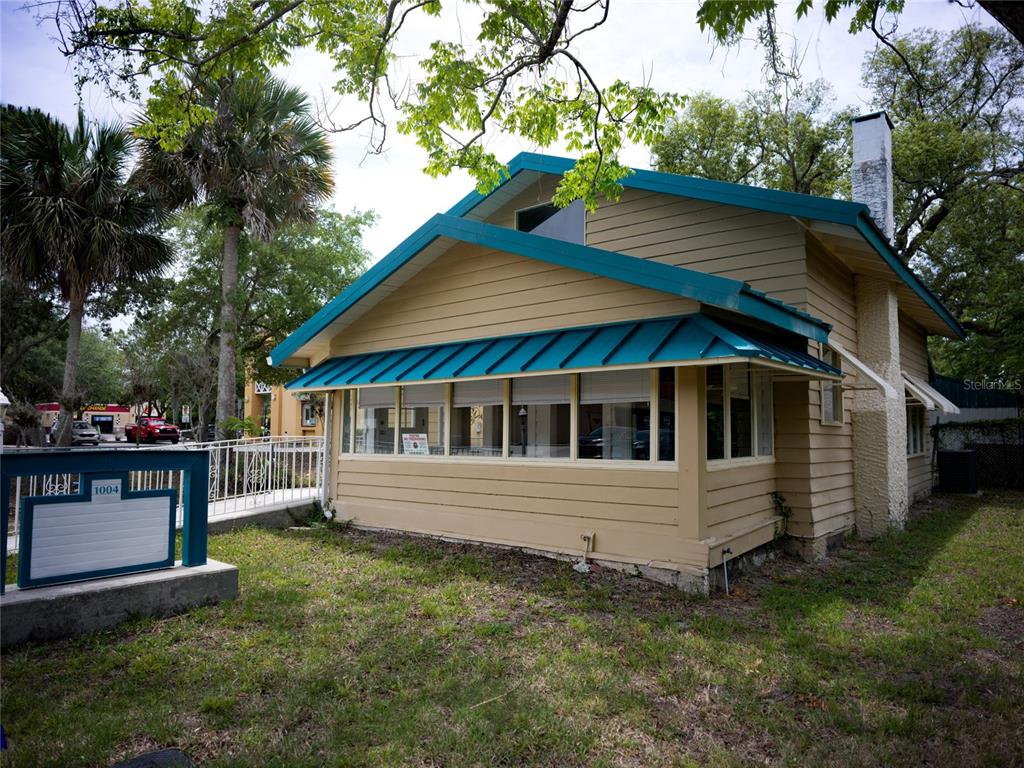 A tan house with a teal metal roof and a wrap-around enclosed porch — 1004 TALTON AVENUE, DELAND, FL