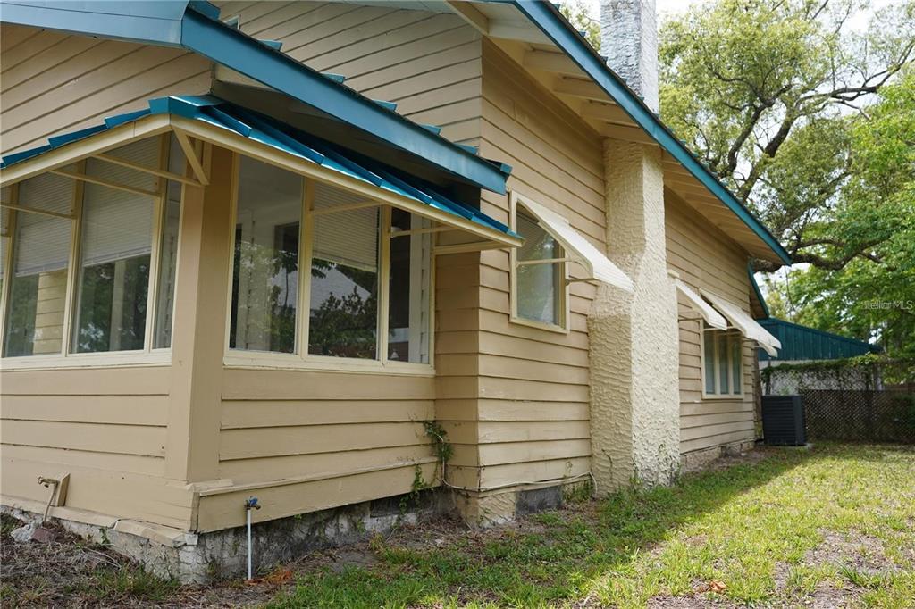 Exterior view of a tan wood-sided house with a stone chimney and teal metal awnings — 1004 TALTON AVENUE, DELAND, FL