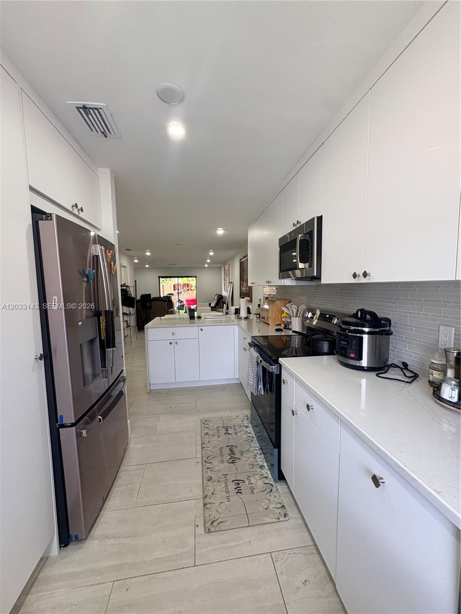 An empty room features white walls, recessed lighting, and light-colored tile flooring leading to a sliding glass door — 15430 SW 74th Cir Ct # 501, Miami FL 33193, MIAMI, FL