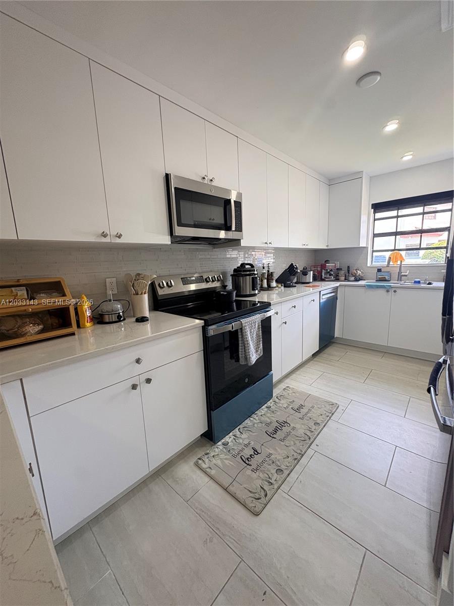 A modern kitchen features white cabinetry, stainless steel appliances, and light-colored tile flooring — 15430 SW 74th Cir Ct # 501, Miami FL 33193, MIAMI, FL