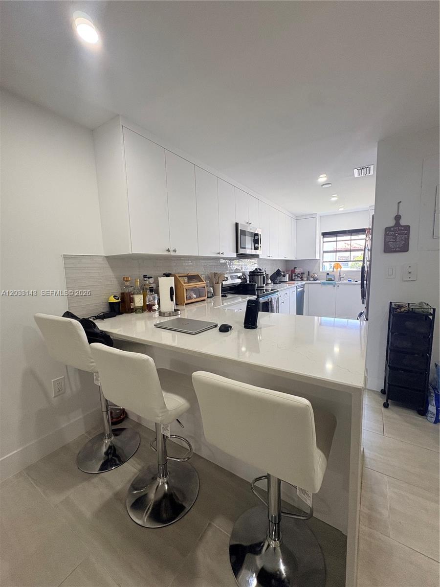 A modern kitchen features white cabinetry, stainless steel appliances, a stacked washer-dryer, and tile flooring — 15430 SW 74th Cir Ct # 501, Miami FL 33193, MIAMI, FL