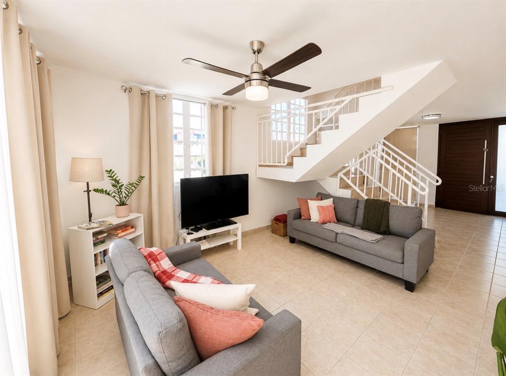 A living room features two gray sofas, a television, and a staircase with white railings — 03 RIO MAMEYES, LUQUILLO, PR