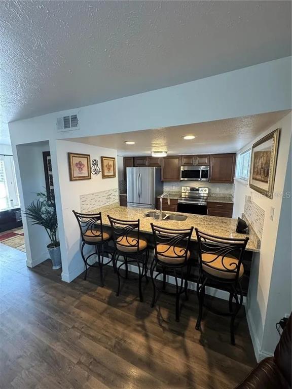 A kitchen features a granite breakfast bar with four stools and dark wood cabinetry — 1836 WARRINGWOOD DRIVE UNIT B4, ORLANDO, FL