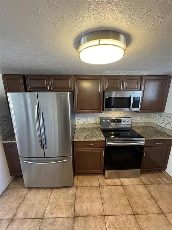 A kitchen features dark wood cabinets, stainless steel appliances, granite countertops, and tiled flooring — 1836 WARRINGWOOD DRIVE UNIT B4, ORLANDO, FL