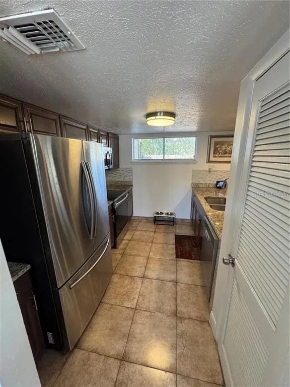 A galley-style kitchen features stainless steel appliances, dark wood cabinetry, and tan floor tiles — 1836 WARRINGWOOD DRIVE UNIT B4, ORLANDO, FL