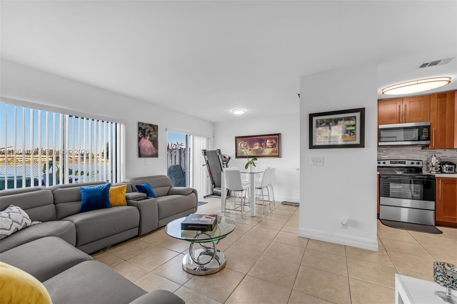 A living room with a grey sectional sofa, glass coffee table, and adjacent dining area — 17501 SW 140th Ct, Miami FL 33177, MIAMI, FL