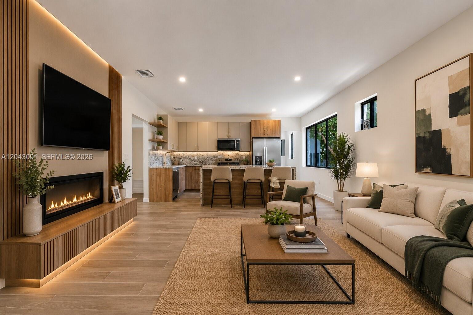 A modern open-concept living room and kitchen featuring wood-look flooring and a linear fireplace — 1020 NW 49th St, Miami FL 33127, MIAMI, FL