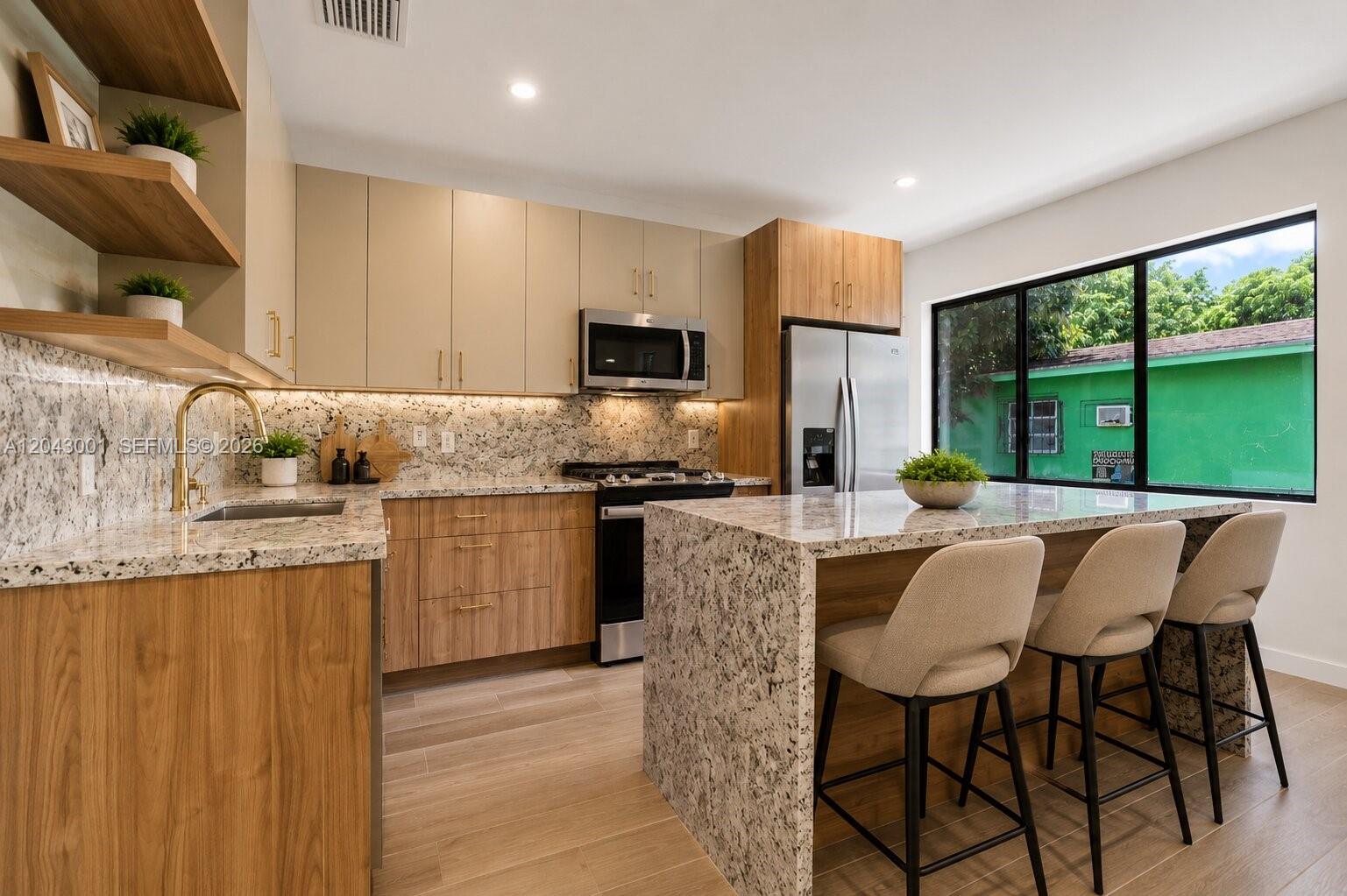 A modern kitchen features wood-tone cabinets, granite countertops, a central island, and three bar stools — 1020 NW 49th St, Miami FL 33127, MIAMI, FL