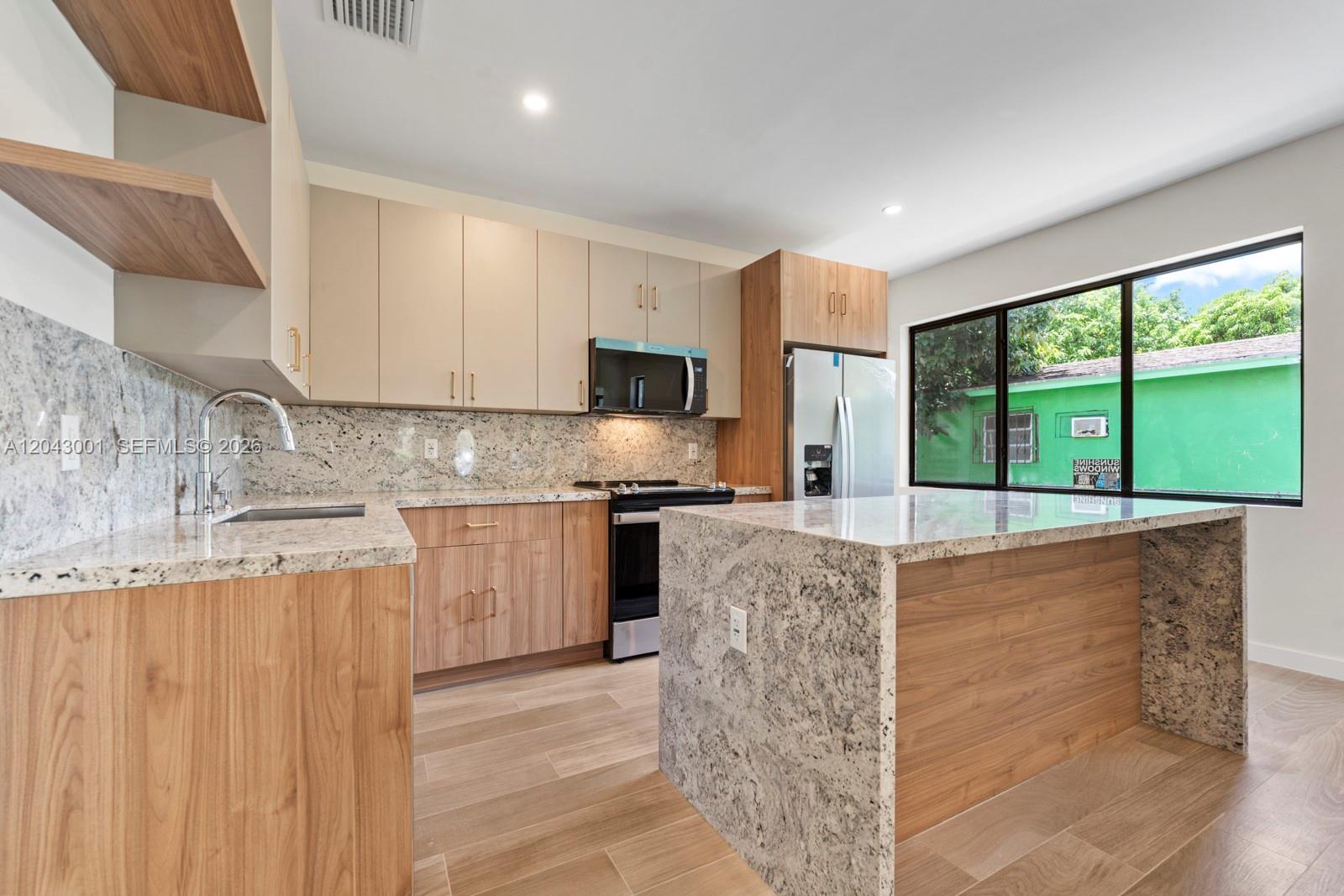 A modern kitchen features wood-tone cabinets, granite countertops, and a large central island — 1020 NW 49th St, Miami FL 33127, MIAMI, FL