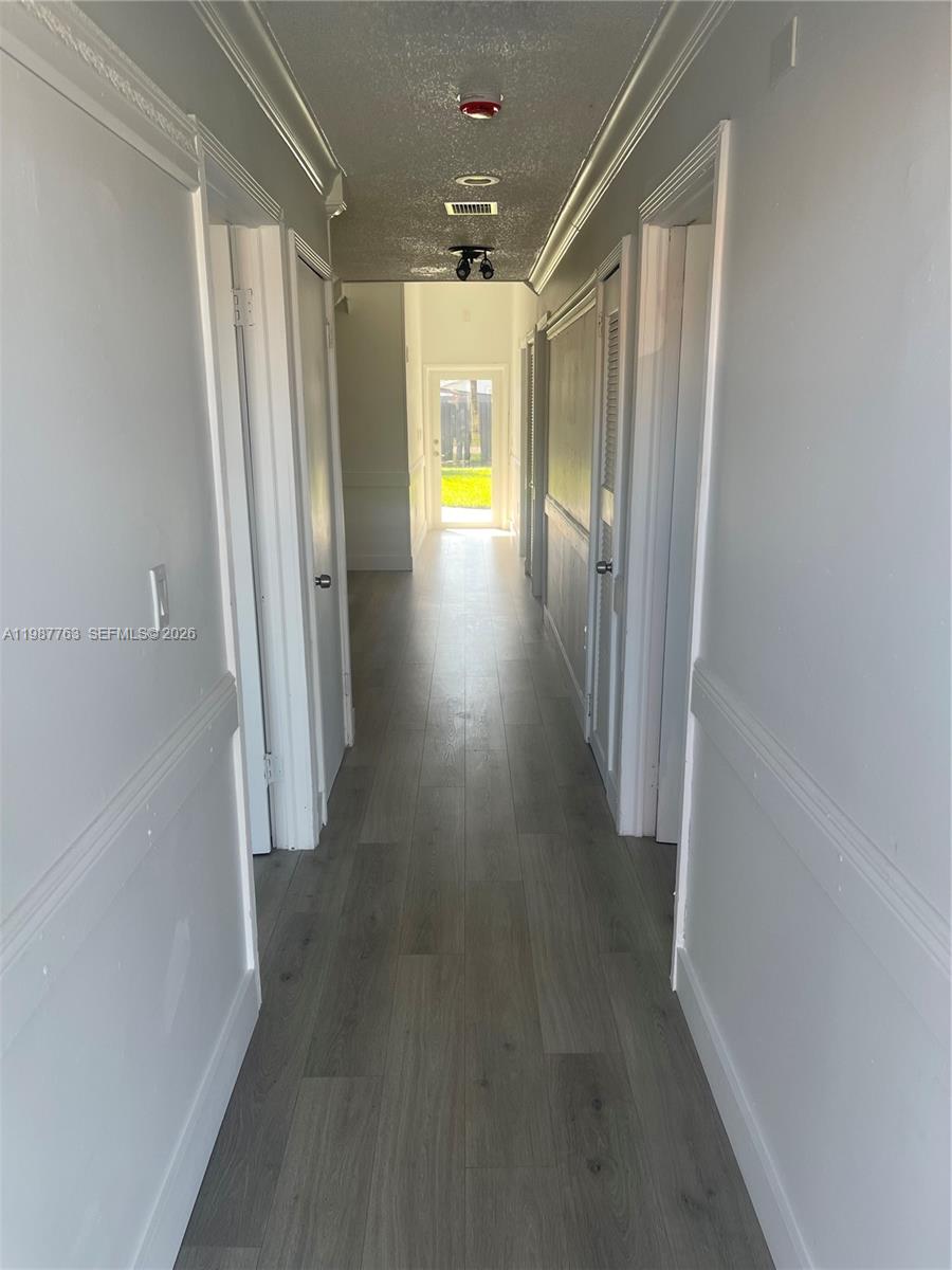 A narrow hallway features light gray wood-look flooring, white walls with wainscoting, and multiple doors — 20700 SW 122nd Ave, Miami FL 33177, MIAMI, FL