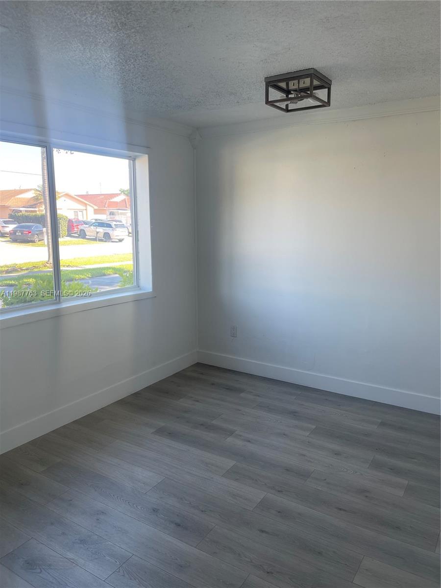 An empty room features white walls, gray wood-look flooring, a window, and a ceiling light — 20700 SW 122nd Ave, Miami FL 33177, MIAMI, FL
