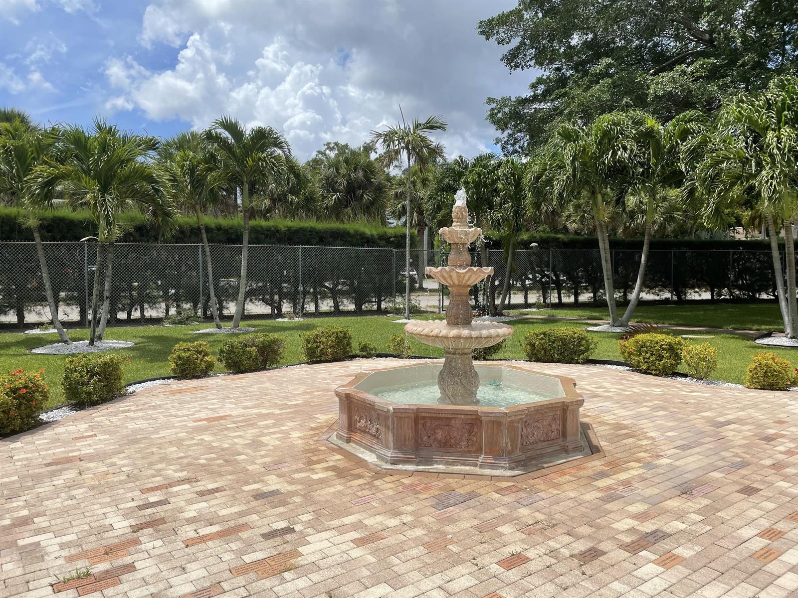 A tiered stone fountain sits in the center of a brick patio surrounded by palm trees — 705 Lori Drive # 315, Palm Springs FL 33461, PALM SPRINGS, FL
