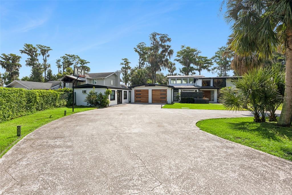 A concrete driveway leads to a modern house with a two-car garage and palm trees — 5583 JESSAMINE LANE, ORLANDO, FL