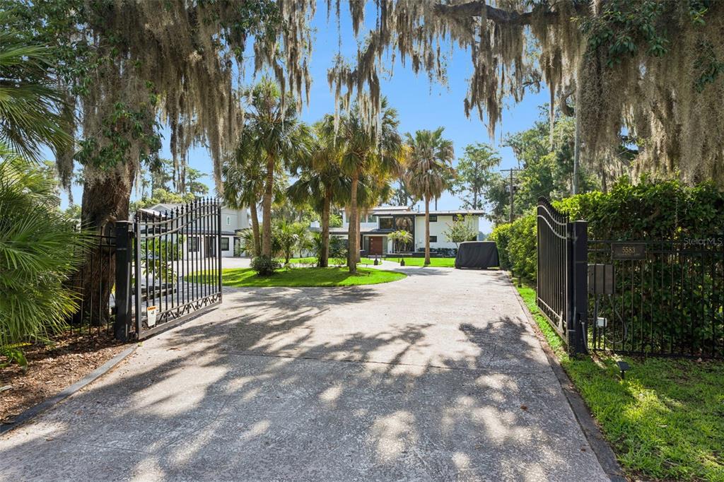 A concrete driveway leads through an open metal gate toward a house with palm trees — 5583 JESSAMINE LANE, ORLANDO, FL