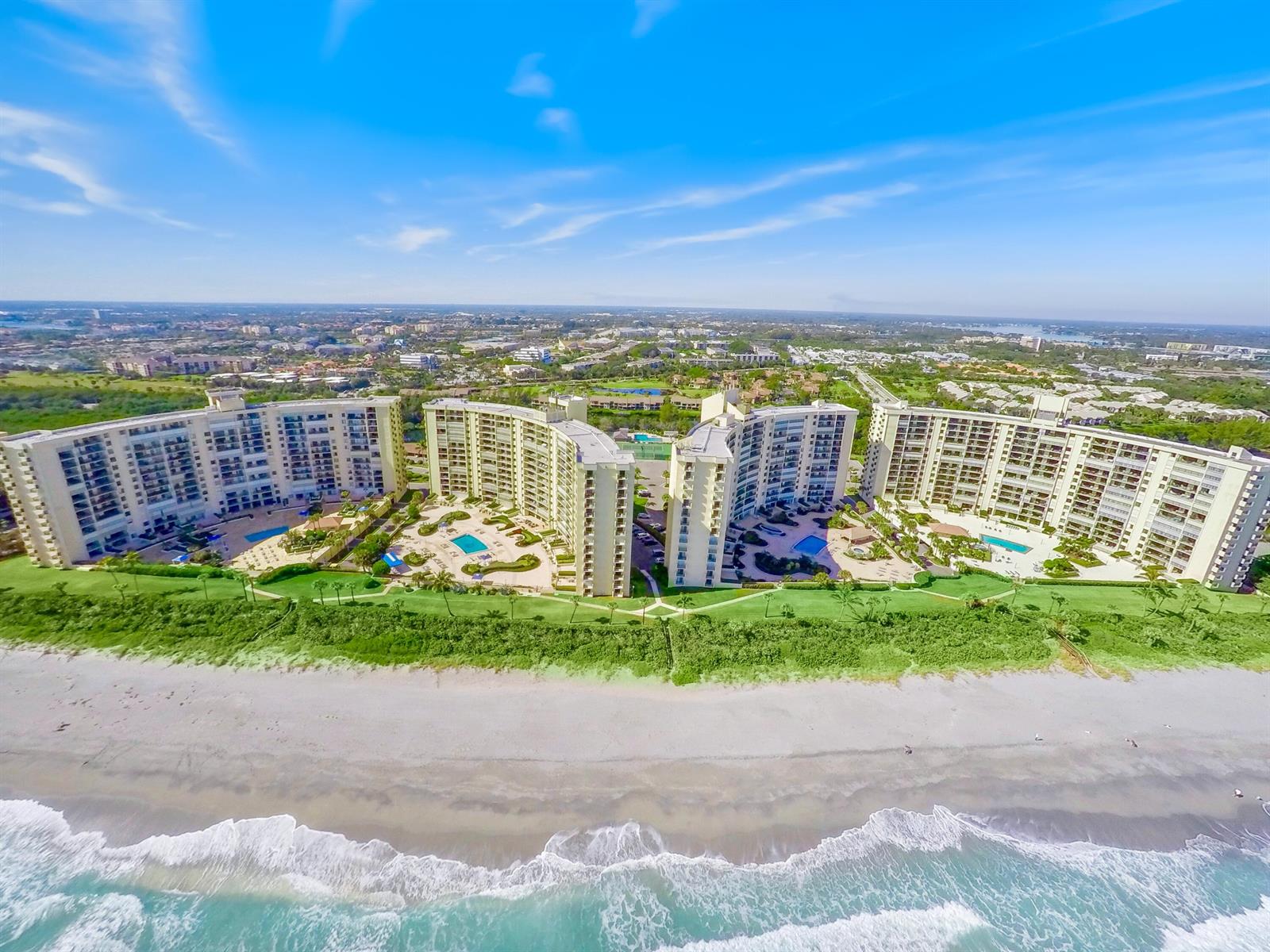 An aerial view shows four curved beachfront condominium buildings with swimming pools and landscaped grounds — 200 Ocean Trail Way # 106, Jupiter FL 33477, JUPITER, FL