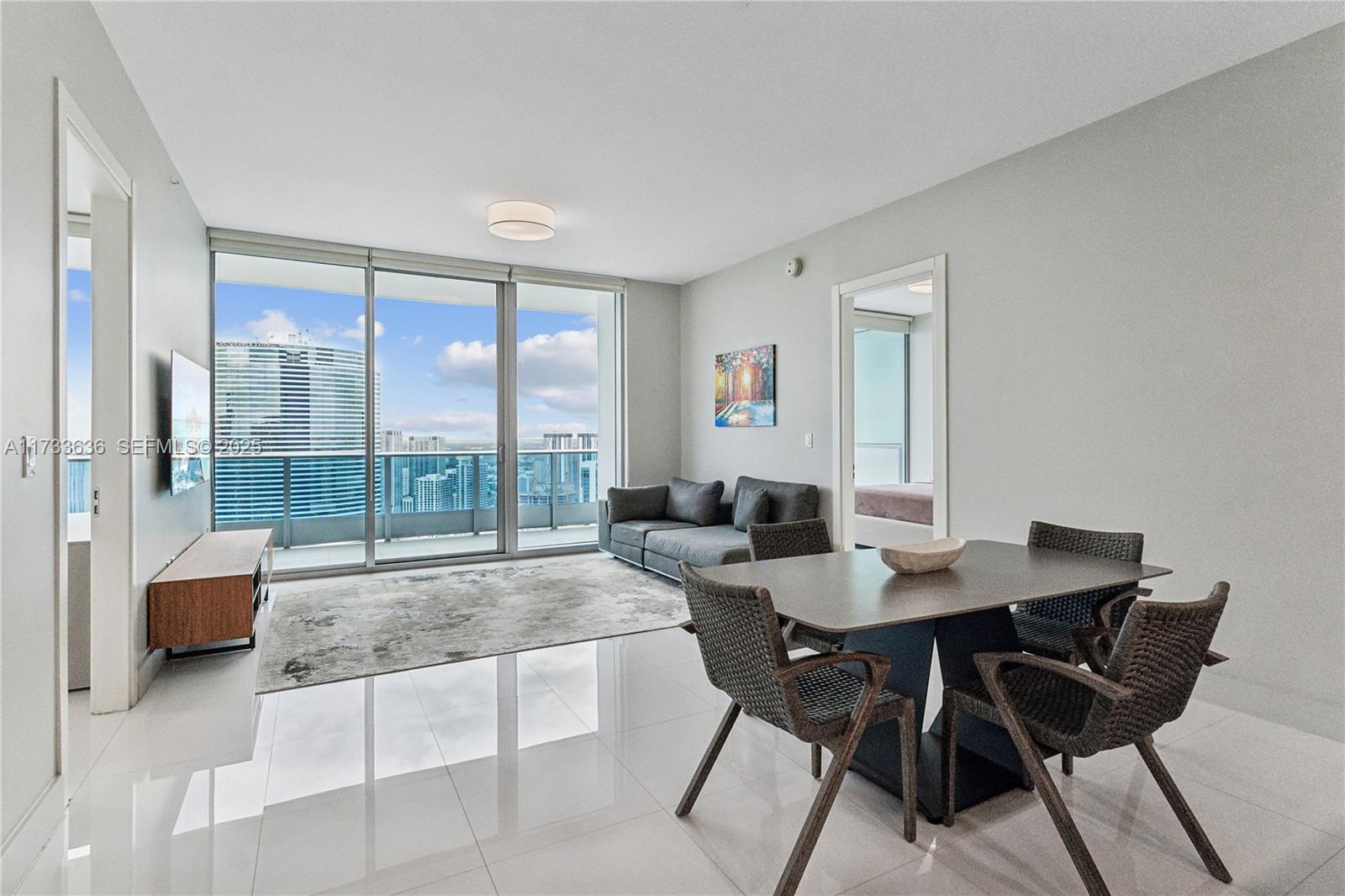 A modern living and dining area features white tile floors, floor-to-ceiling windows, and city views — 200 Biscayne Boulevard Way # 4912, Miami FL 33131, MIAMI, FL