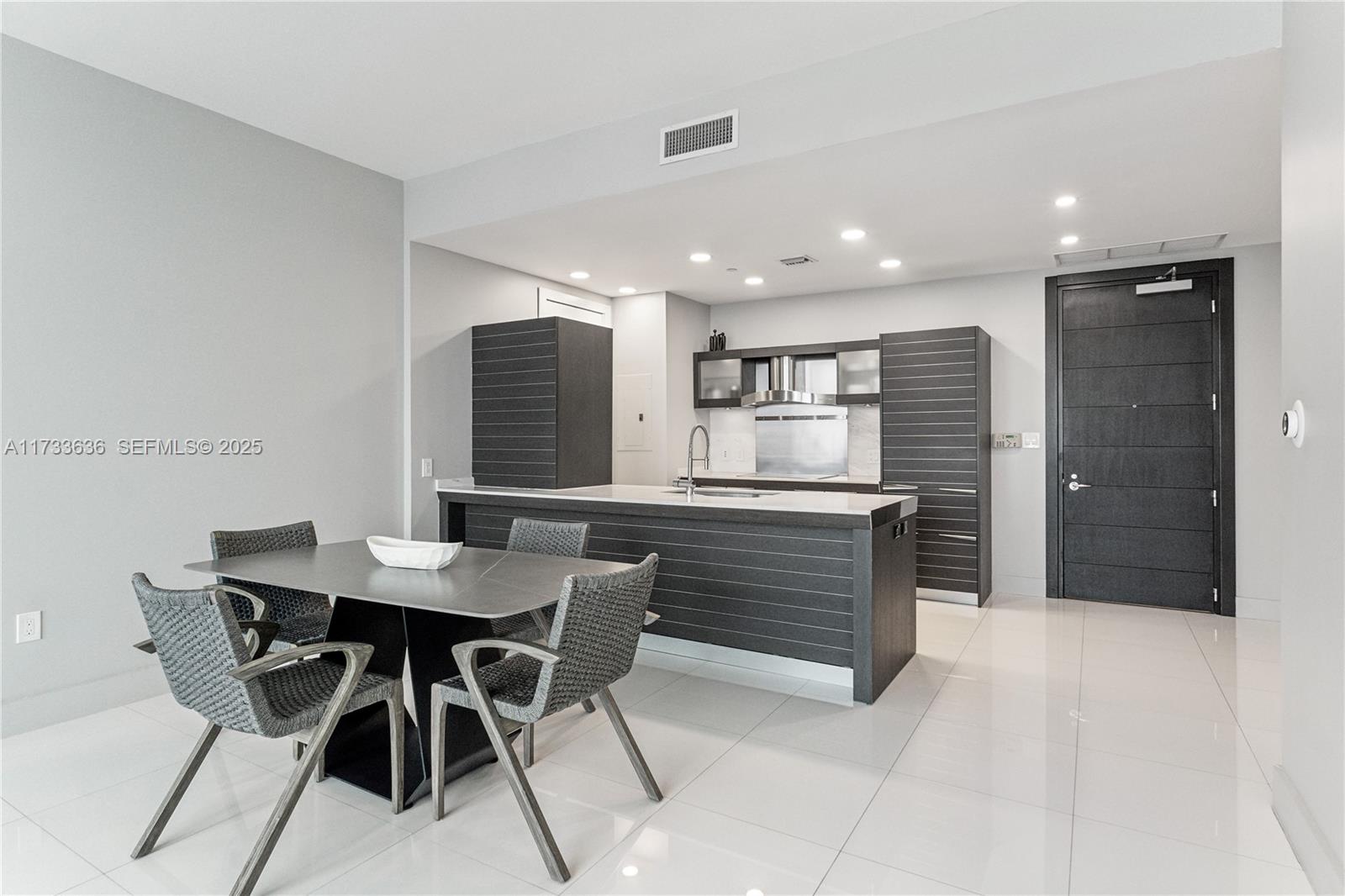 A modern kitchen with dark cabinetry and a dining table sits on white tiled floors — 200 Biscayne Boulevard Way # 4912, Miami FL 33131, MIAMI, FL