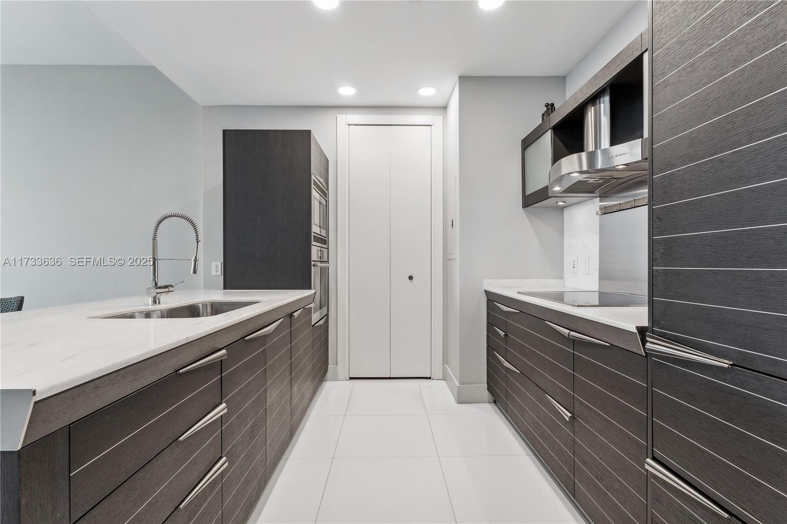 A modern galley kitchen features dark wood cabinets, white countertops, and stainless steel appliances — 200 Biscayne Boulevard Way # 4912, Miami FL 33131, MIAMI, FL