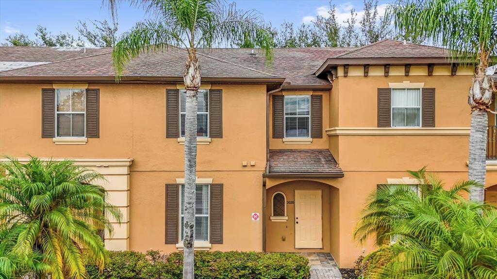 A two-story tan stucco townhouse with brown shutters, a tiled roof, and palm trees — 2020 CALABRIA AVENUE, DAVENPORT, FL