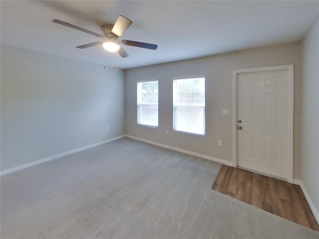 An empty room features gray carpet, light gray walls, a ceiling fan, and a side door — 2491 STANTON AVENUE, SPRING HILL, FL