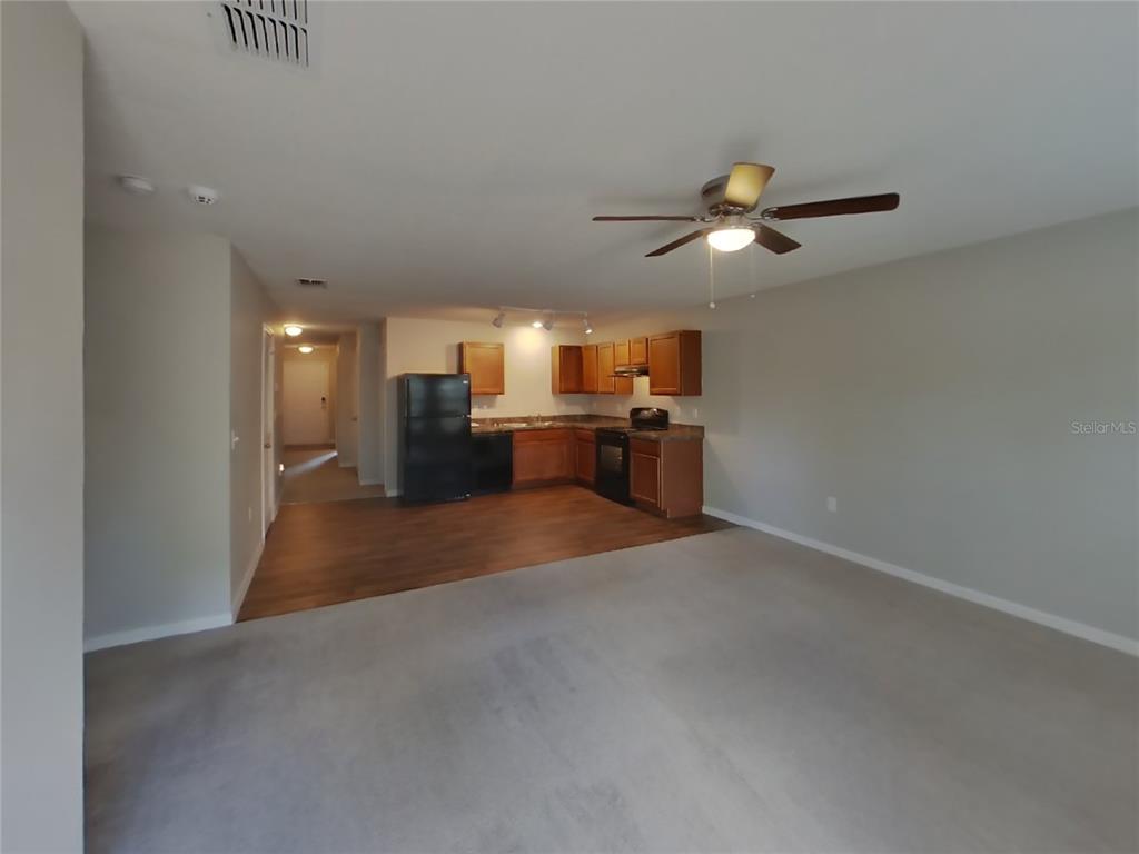 An open-concept living area features a carpeted floor, a ceiling fan, and a kitchen area — 2491 STANTON AVENUE, SPRING HILL, FL