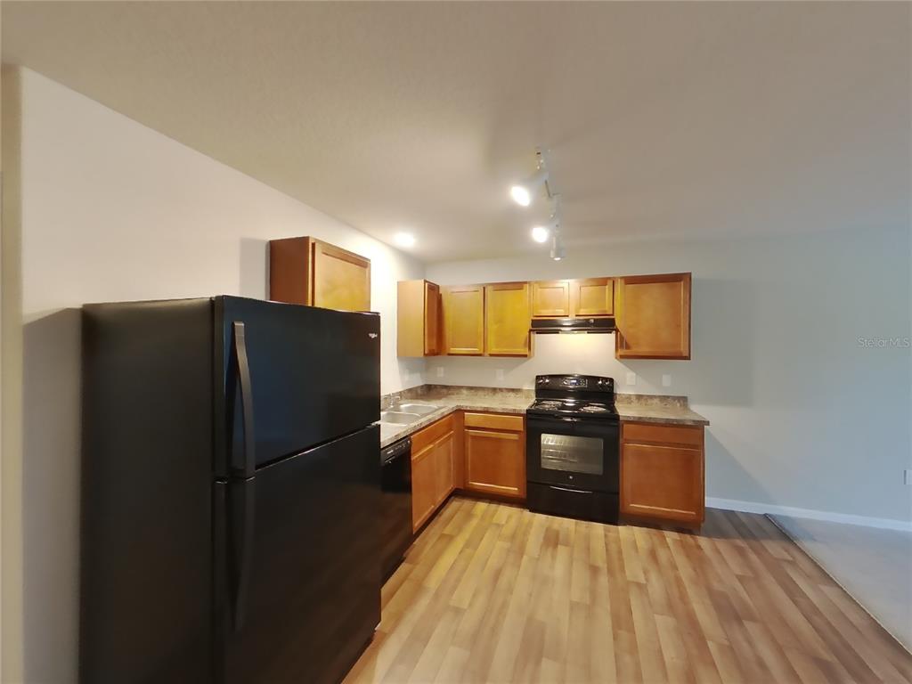 A kitchen features wood cabinets, black appliances, laminate countertops, and light-colored wood-look flooring — 2491 STANTON AVENUE, SPRING HILL, FL