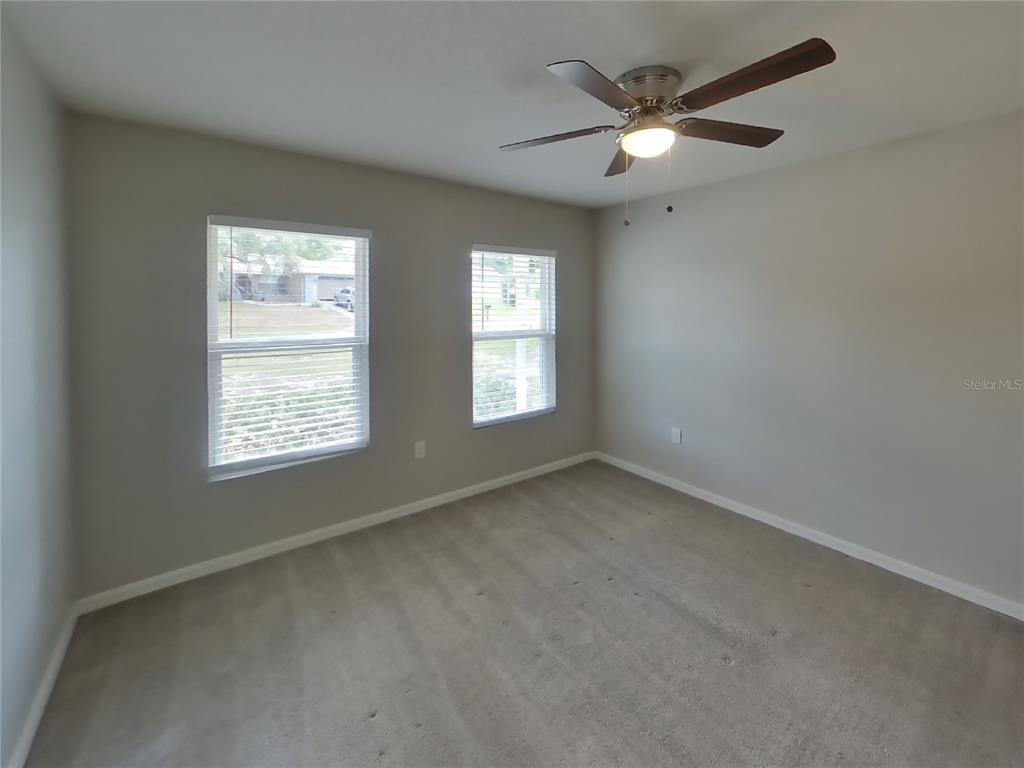 An empty bedroom features light gray walls, beige carpeting, two windows, and a ceiling fan — 2491 STANTON AVENUE, SPRING HILL, FL