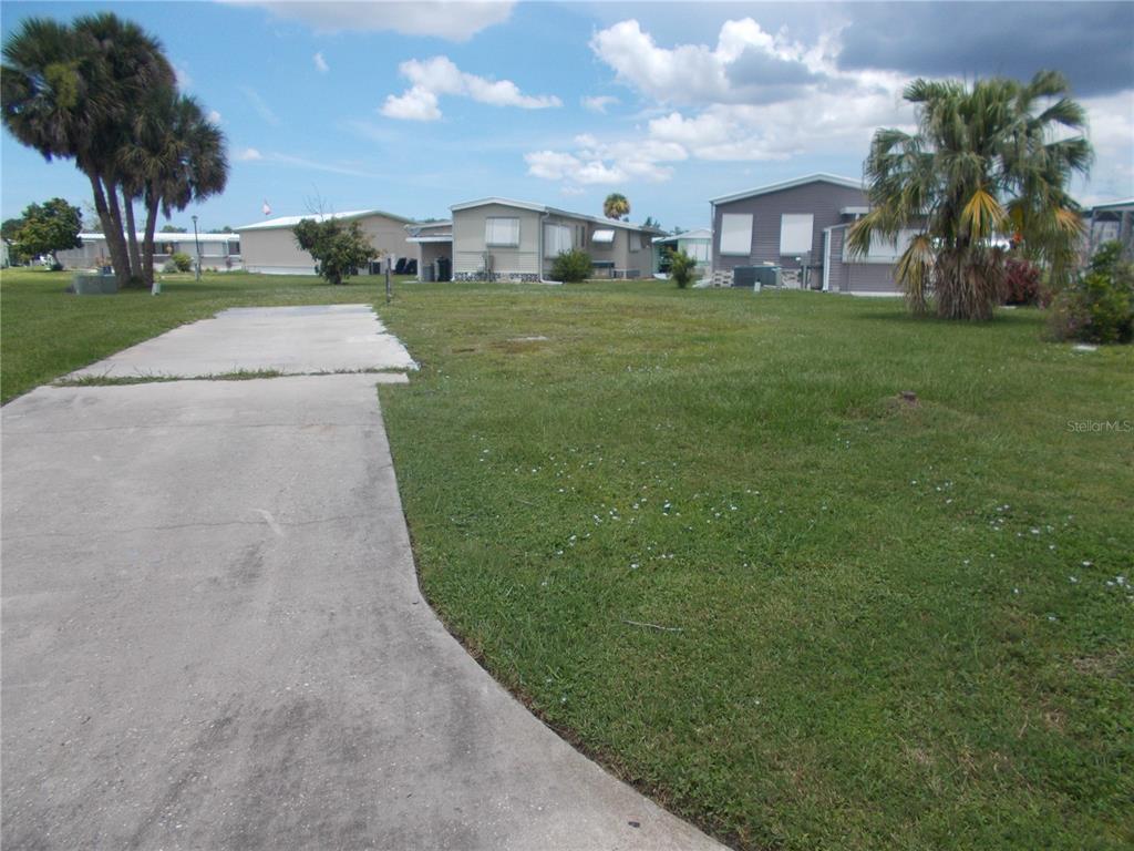 A concrete driveway leads to a grassy lot with palm trees and neighboring mobile homes — 6786 NEIGHBORLY COURT, NORTH PORT, FL