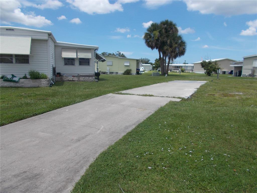 A concrete driveway leads toward a light-colored mobile home on a grassy lot — 6786 NEIGHBORLY COURT, NORTH PORT, FL