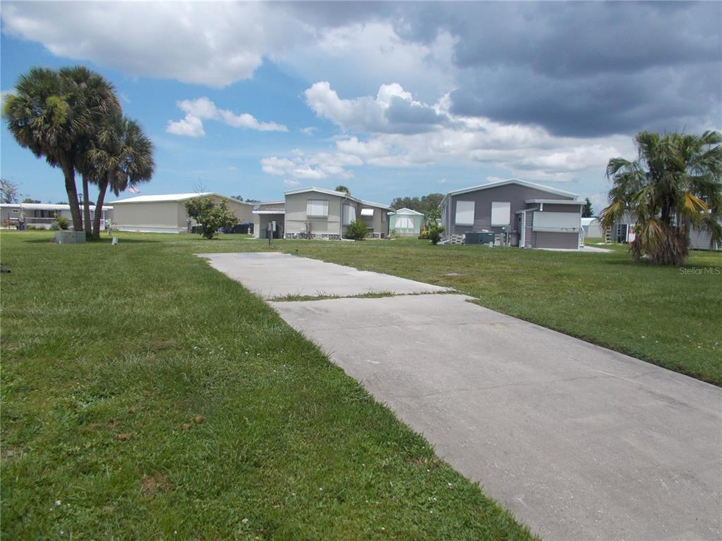 A concrete driveway leads toward several manufactured homes on a grassy lot under a cloudy sky — 6786 NEIGHBORLY COURT, NORTH PORT, FL